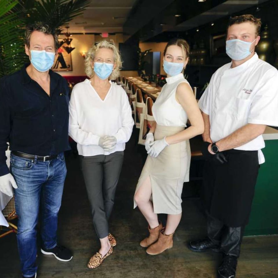 Four restaurant staff members, including a chef, wearing face masks and gloves inside a dining room.