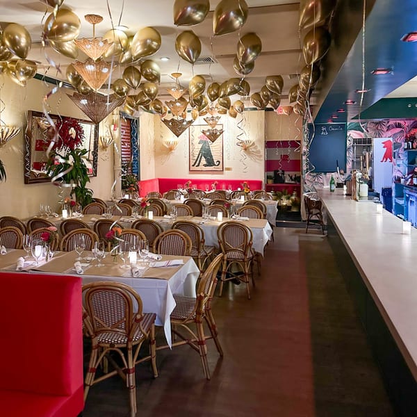 A festive restaurant dining room with tables set, red booths, and gold balloons on the ceiling.
